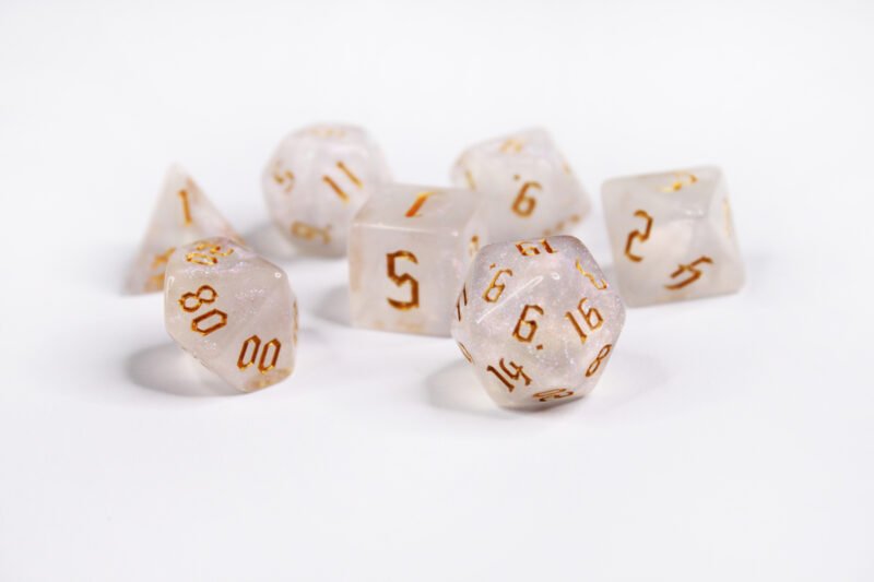 Collection of seven acrylic dice with fine glittery off-white colouring and gold numbers