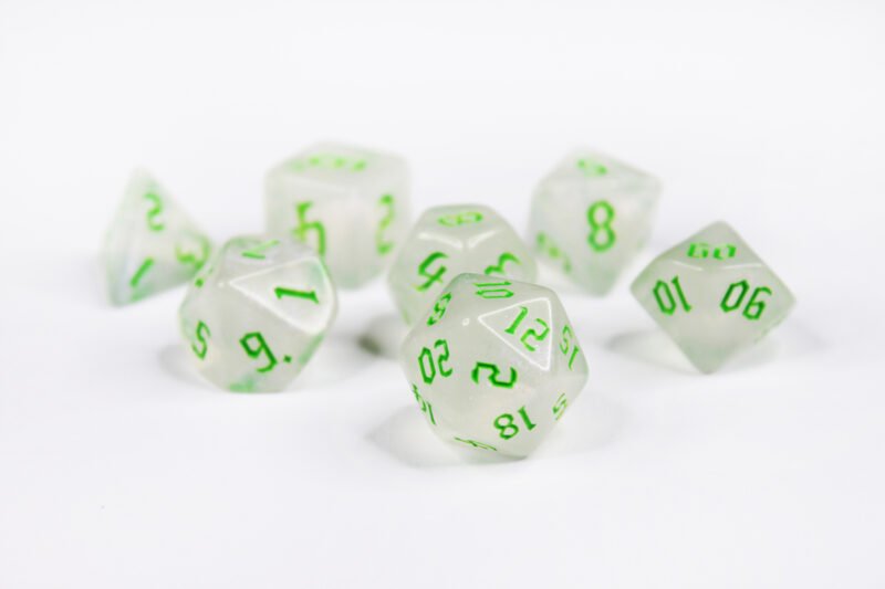 Collection of seven acrylic dice with fine glittery off-white colouring and green numbers