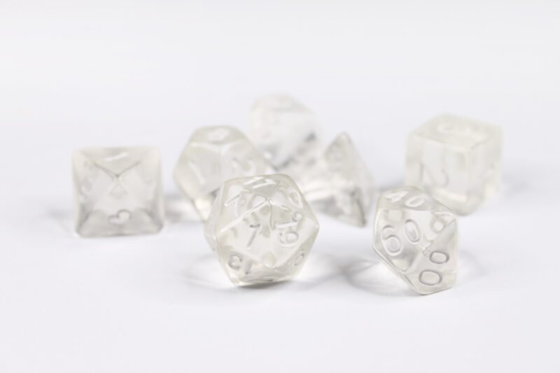 Collection of seven acrylic dice with of clear colouring and white numbers giving them an invisible illusion
