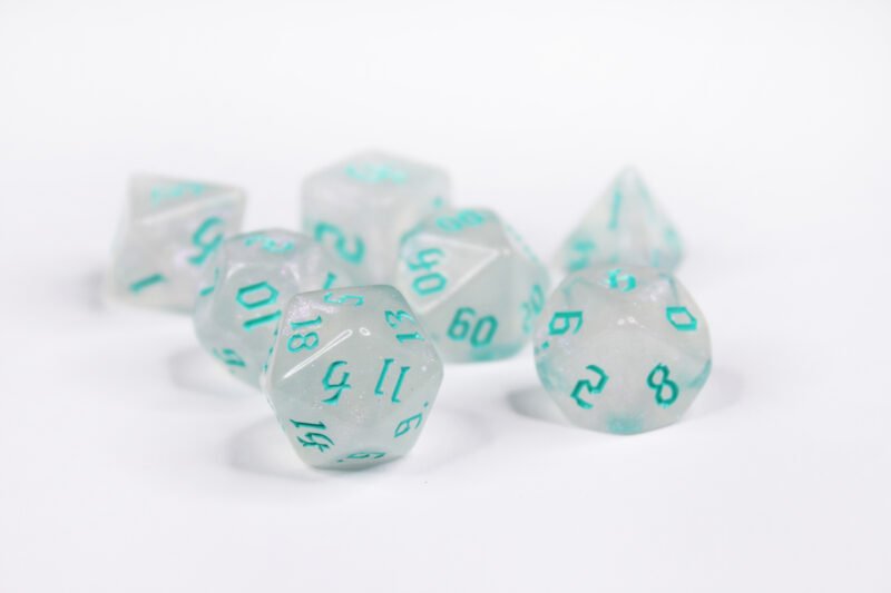 Collection of seven acrylic dice with fine glittery off-white colouring and sea foam blue numbers