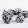Collection of seven black dice with embossed swirling patterns and white coloured motif and numbering