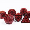 Collection of seven black dice with embossed swirling patterns and red coloured motif and numbering