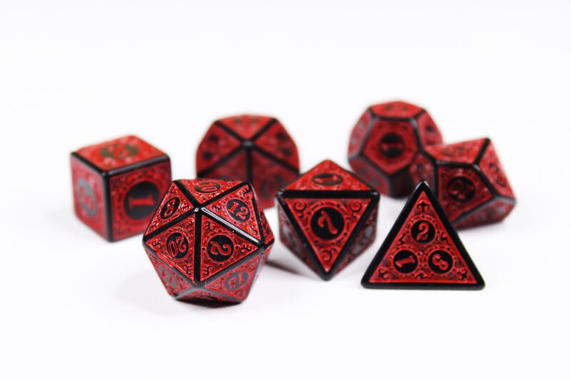 Collection of seven black dice with embossed swirling patterns and red coloured motif and numbering