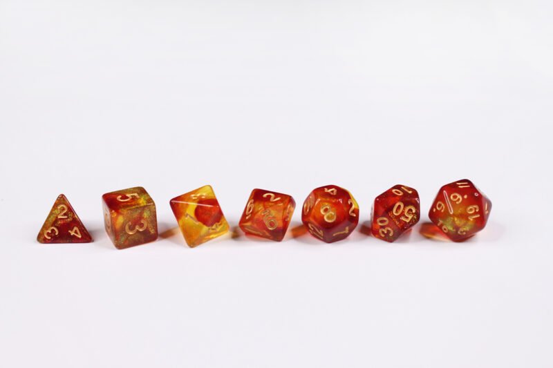 Collection of seven acrylic dice with swirled fine glittery red and yellow colouring and gold numbers