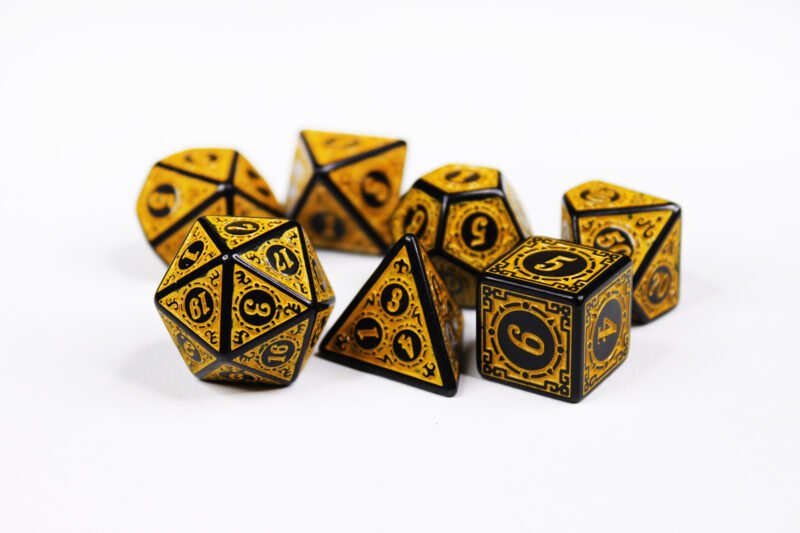 Collection of seven black dice with embossed swirling patterns and yellow coloured motif and numbering