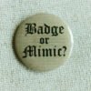 A beige coloured button badge showing the text “Badge or Mimic” in a medieval Blackletter font sitting on cream coloured textile.