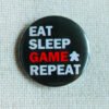 A black button badge showing the text Eat Sleep Game Repeat and the Meeple Silhouette. The word game is in red, the rest in white.