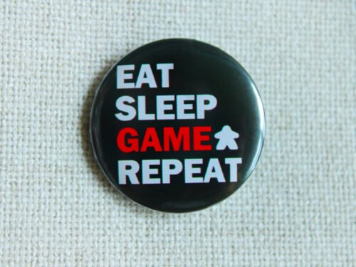 A black button badge showing the text Eat Sleep Game Repeat and the Meeple Silhouette. The word game is in red, the rest in white.