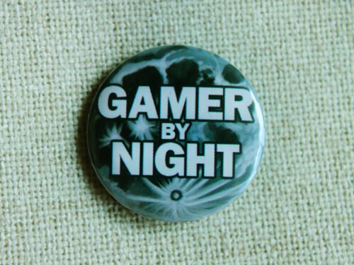 A button badge showing a full moon and the text Gamer By Night across it in white.