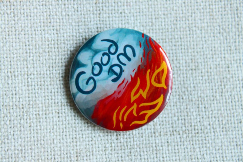 An illustrated button badge with one half that shows blue sky and clouds and text that reads Good DM and another half that shows flames and the text Evil DM.