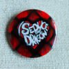 A button badge showing red reptilian scales and the text I Seduce the Dragon across a classic shaped heart.