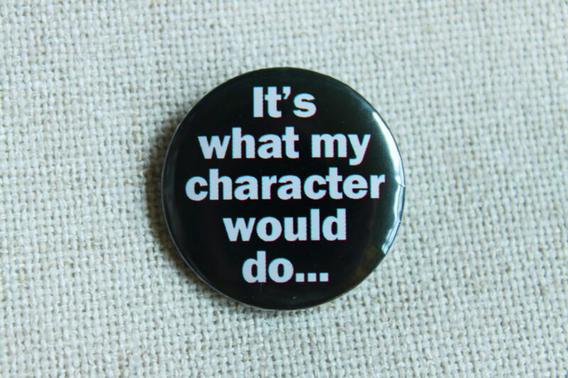 A black coloured button badge which reads the text "It's what my character would do..." in white lettering.