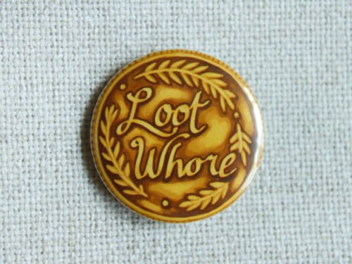 A gold coloured button badge illustrated to look like a coin with the text Loot Whore on it and decorative leaves.