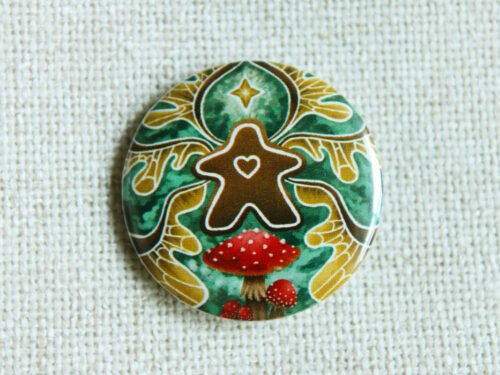 A button badge of a gingerbread meeple with faerie wings a star and fly agaric toadstools