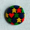 A black button badge with rows of meeple silhouettes in the colours red yellow green and blue and a classic shaped red heart.