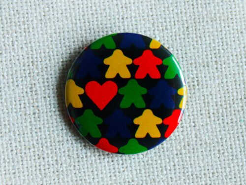 A black button badge with rows of meeple silhouettes in the colours red yellow green and blue and a classic shaped red heart.