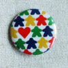 A white button badge with rows of meeple silhouettes in the colours red, yellow, green and blue and a classic shaped red heart.