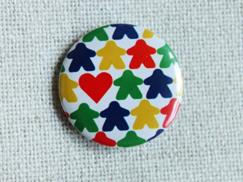 A white button badge with rows of meeple silhouettes in the colours red, yellow, green and blue and a classic shaped red heart.