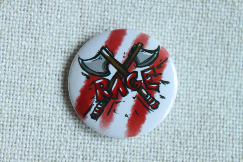 A white button badge with three red stripes, two illustrated hand axes crossed in an x, and the hand drawn text RAGE in red.