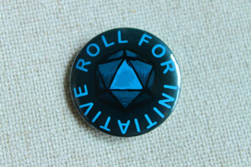 A dark blue button badge with turquoise coloured text reading Roll for Initiative and a centrally an illustrated D20