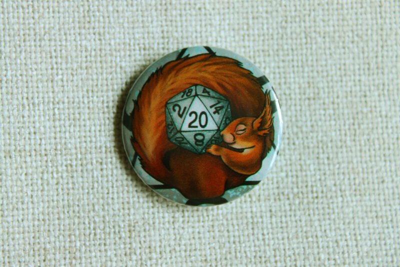 A button badge showing a European red squirrel curled around a grey coloured D20 Die