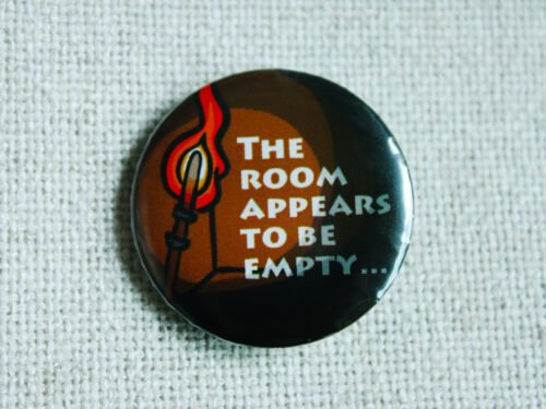 An illustrated button badge showing a fire torch and a dark empty room with the text The Room Appears to be Empty