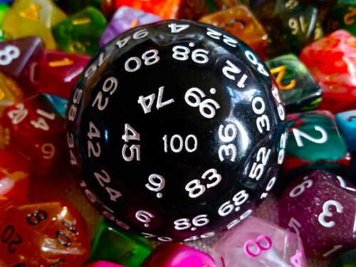 A large 100-sided die in black with white numbers resting on a bed of colourful polyhedral dice.