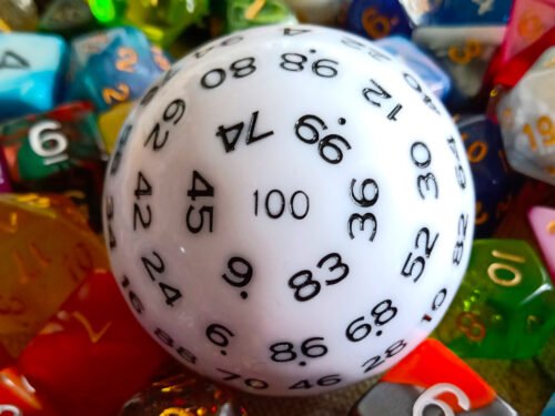 A large 100-sided die in white with black numbers resting on a bed of colourful polyhedral dice.