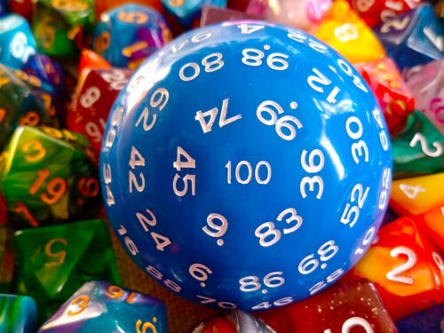 A large 100-sided die in blue with white numbers resting on a bed of colourful polyhedral dice.