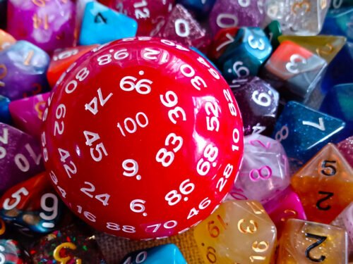 A large 100-sided die in red with white numbers resting on a bed of colourful polyhedral dice.