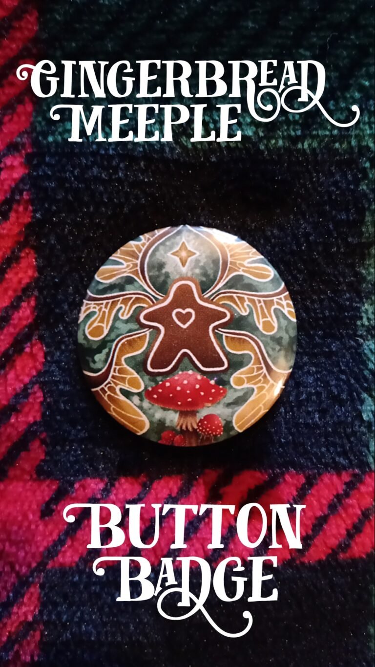 A button badge of a gingerbread meeple with faerie wings lying on a plaid patterned blanket.