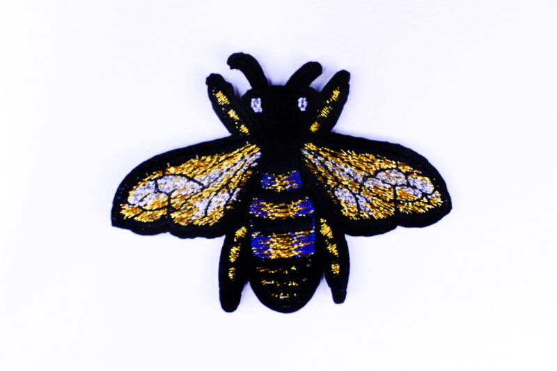 An embroidered patch of a bee in the colours black, gold and blue.