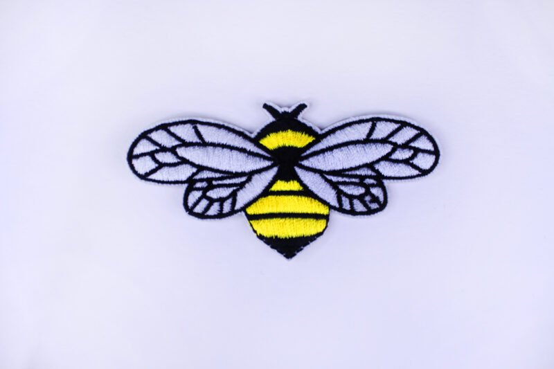 An embroidered patch of a bee with widespread wings in the colours white, black and yellow.