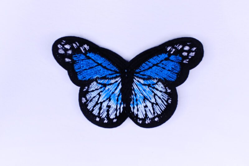 An embroidered patch of a butterfly in the style of a monarch butterfly but in the colours black white and blue.