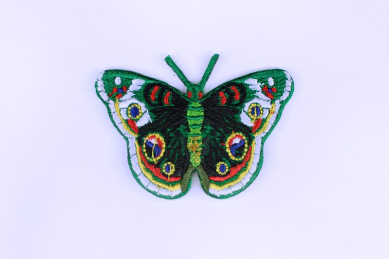 An embroidered patch of a green butterfly with white black blue red and yellow markings.