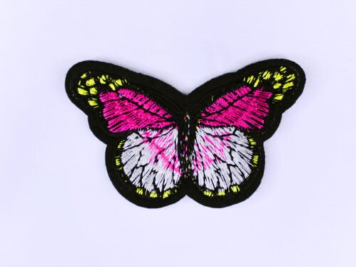 An embroidered patch of a butterfly in the style of a monarch butterfly but in the colours black white pink and yellow.