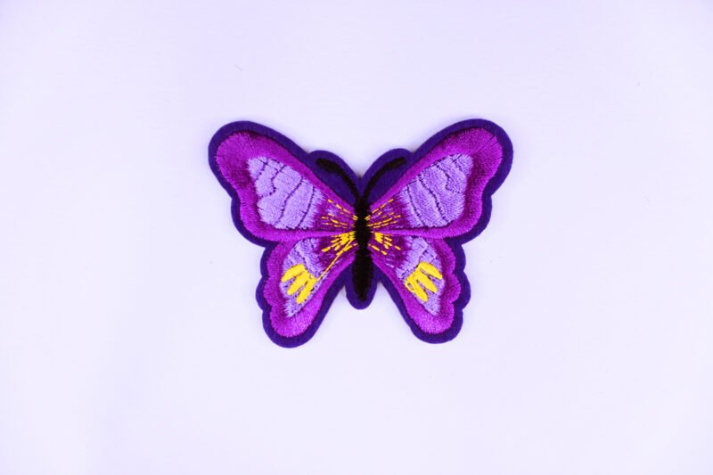 An embroidered patch of a purple butterfly with yellow and light purple markings.