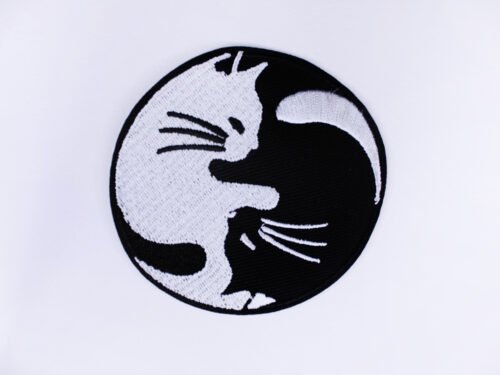 An embroidered patch of a ying yang symbol made up of a black and a white cat cuddling.