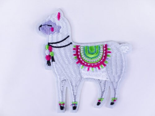 An embroidered patch of a white llama wearing a colourful saddle with tassels and other tasseled accessories.