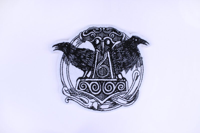 An embroidered patch stitched in a very sketchy manner. It is of the viking symbol Mjollnir flanked by two ravens.