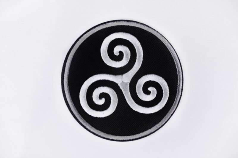 An embroidered patch of a Celtic triskele in the colours black white and grey