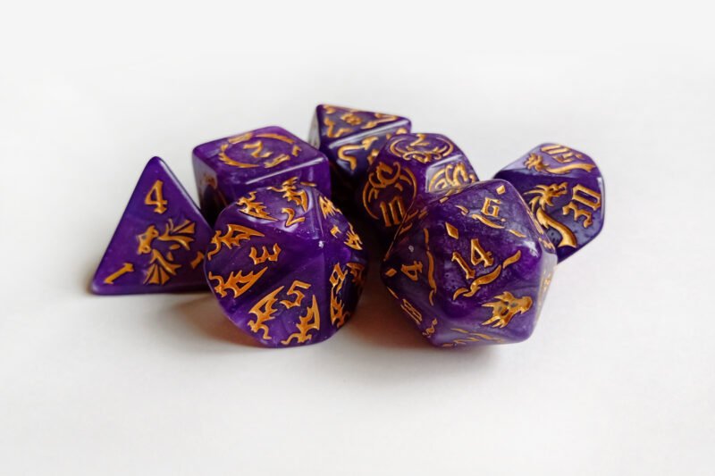 Collection of seven purple dice with embossed dragon patterns and gold coloured motif and numbering.