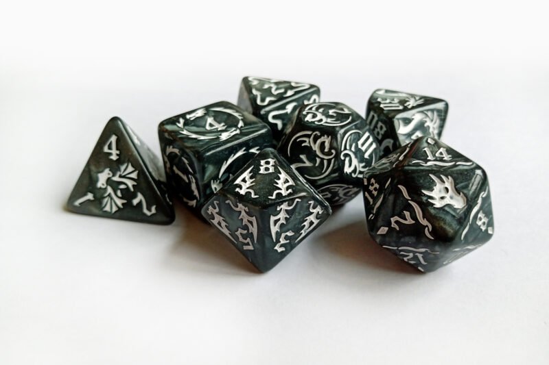 Collection of seven dark grey dice with embossed dragon patterns and white coloured motif and numbering.