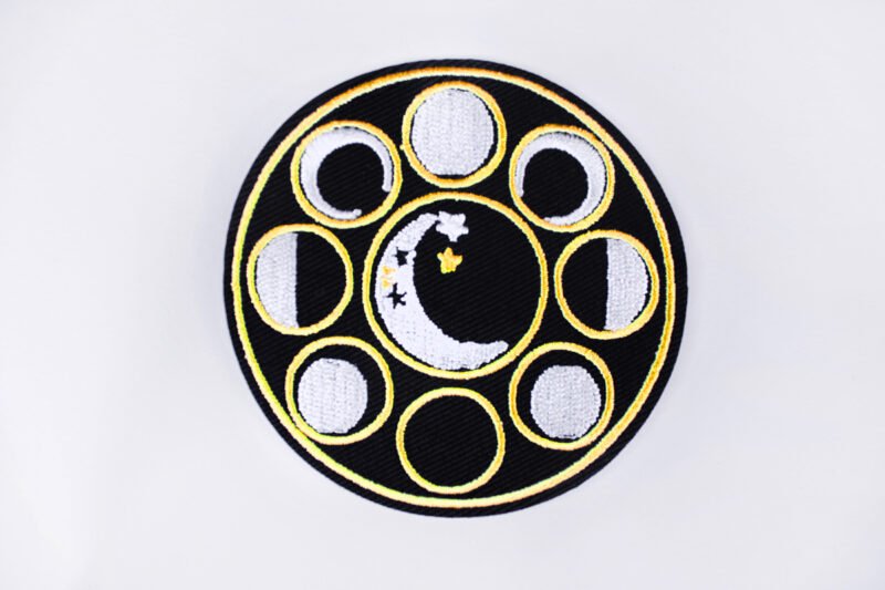 An embroidered patch of a crescent moon with stars encircled by eight different moon phases.