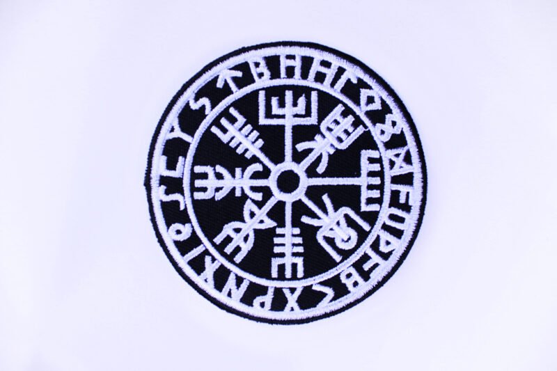 A circular embroidered patch of a the Norse compass Vegvisir encircled by viking runes in black and white